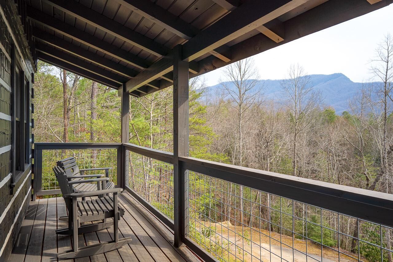 A covered porch with two Adirondack chairs, a view of a forested mountain range.