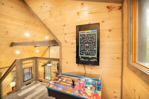 A wooden interior with a game table, a monitor displaying a maze game, and a staircase. - Trail's End (Gatlinburg)