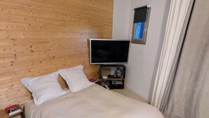 Quarto com cama, televisão, cabeceira de madeira, mesa de cabeceira e janela com cortinas.