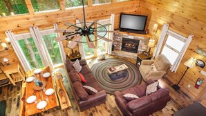 Ein Blockhaus-Interieur mit Holzboden, Kamin, Fernseher, einer Couch und einem Esstisch.