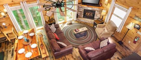 A cabin interior with a wooden floor, a fireplace, a television, a sofa, and a dining table.