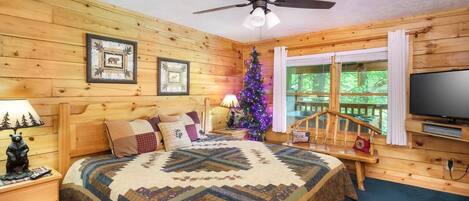 Een gezellig slaapkamer in chaletstijl met een bed, houten wanden, een plafondventilator, een kerstboom en een televisie.
