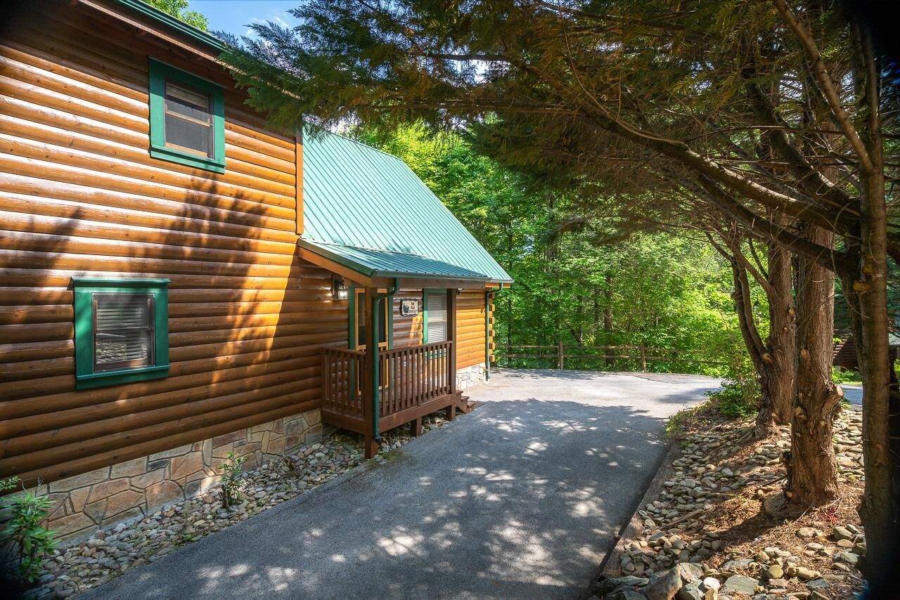 A log cabin with a stone foundation, a porch, and a metal roof.