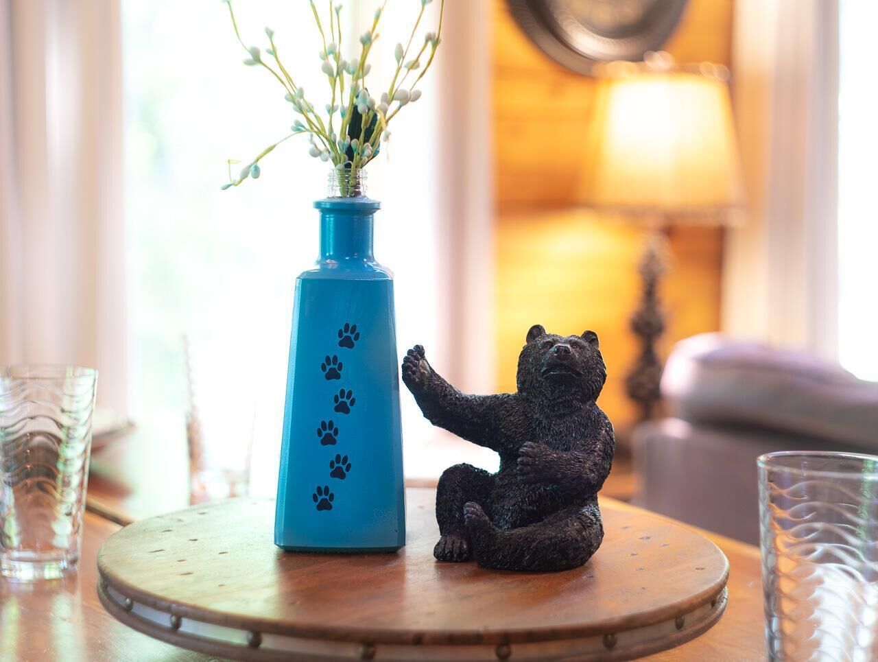 Un vase bleu orné d’empreintes de pattes et une figurine d’ours, posés sur une table ronde en bois.