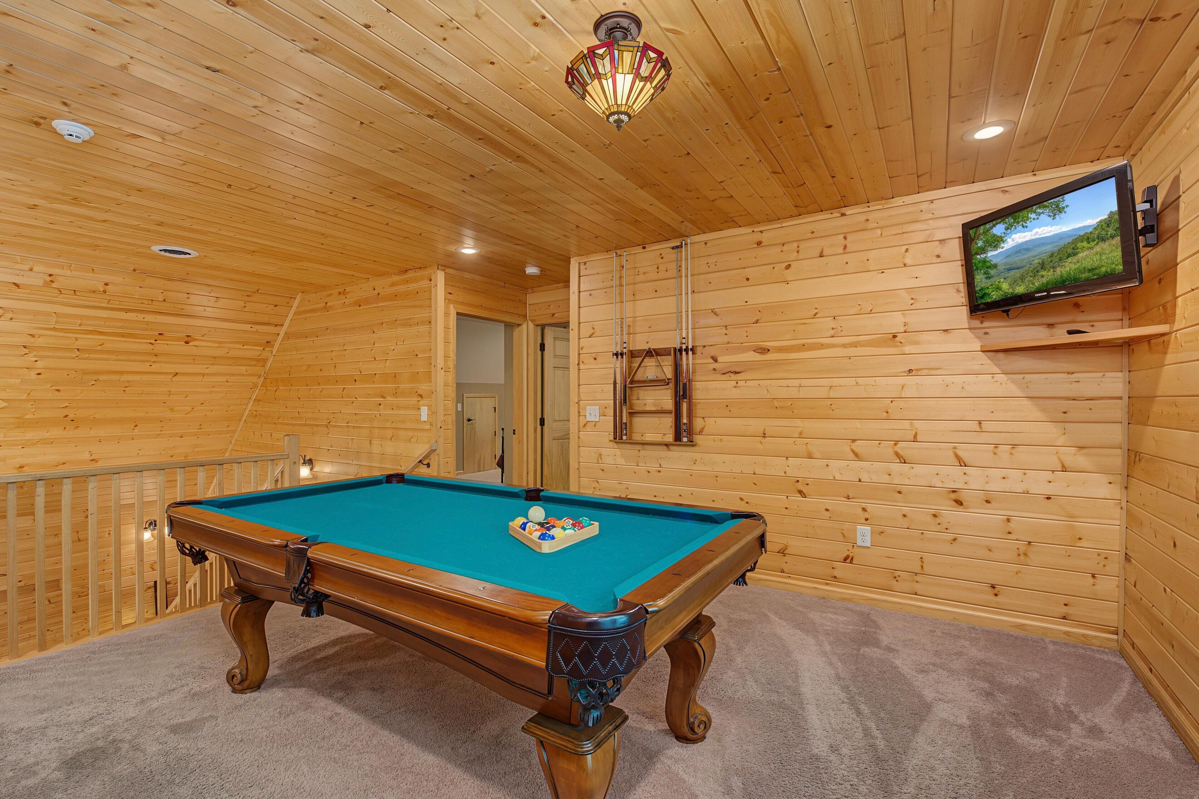 A pool table with a mounted television in a wooden-paneled room.