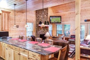 A wooden cabin interior with a kitchen island, dining area, and seating. - Cork's Creekside (Cosby)