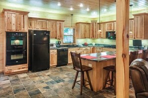 Eine Küche mit Holzausstattung, einem Kühlschrank, einem Backofen, einer Mikrowelle, einer Kaffeemaschine und einer Bar mit Hockern.