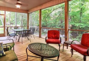 A covered outdoor area with a table and chairs, large windows, and a view of a forest. - Cork's Creekside (Cosby)