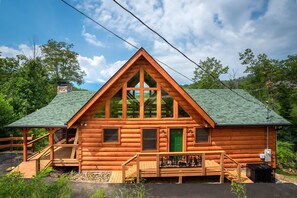 Eine Blockhütte mit einem grünen Dach, einer Veranda und einem Schornstein.