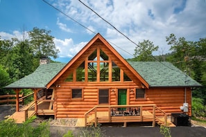 A log cabin with a green roof, a front porch, and a chimney. - Four Bears (Gatlinburg)