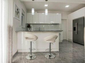 A modern kitchen with white cabinets, stainless steel appliances, and two bar stools. - Villa Antonija With Outdoor Pool (Imotski)