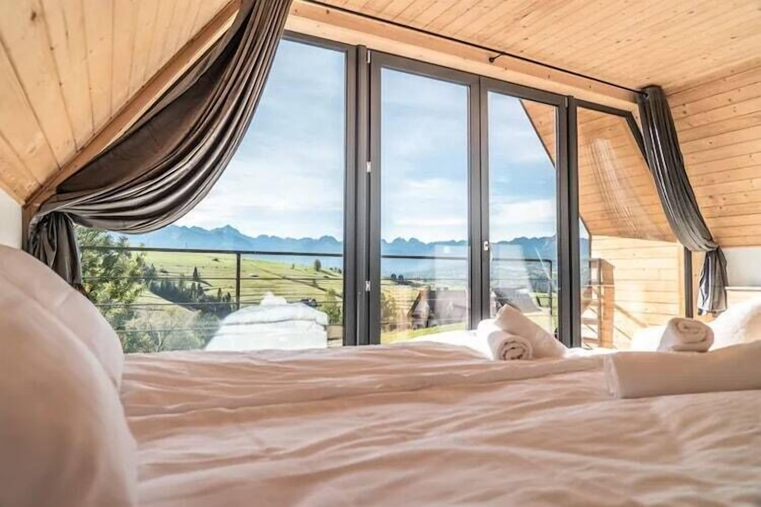 Une chambre dotée d’un grand lit, d’un plafond en bois et offrant une vue sur un paysage montagneux grâce à de grandes fenêtres.