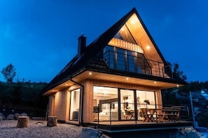 Une maison moderne dotée d’une grande façade vitrée, d’un balcon et d’une façade extérieure en bois.