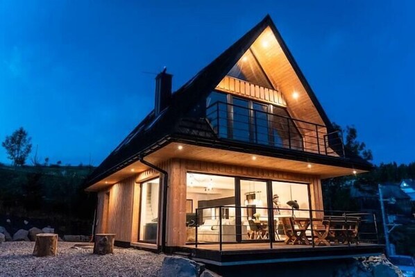 Een modern huis met een grote glazen voorgevel, een balkon en een houten gevel.