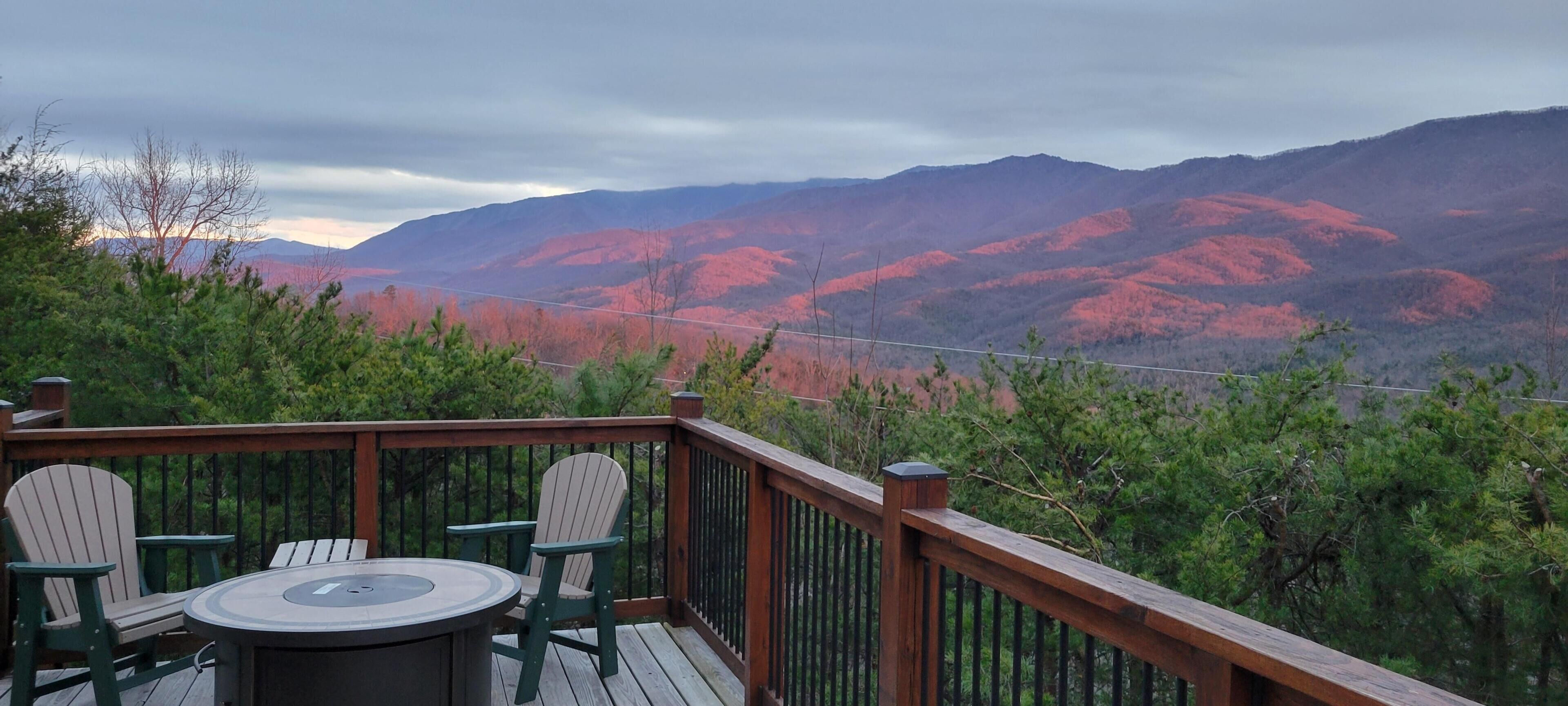 A deck with chairs and a table, overlooking a mountainous landscape.