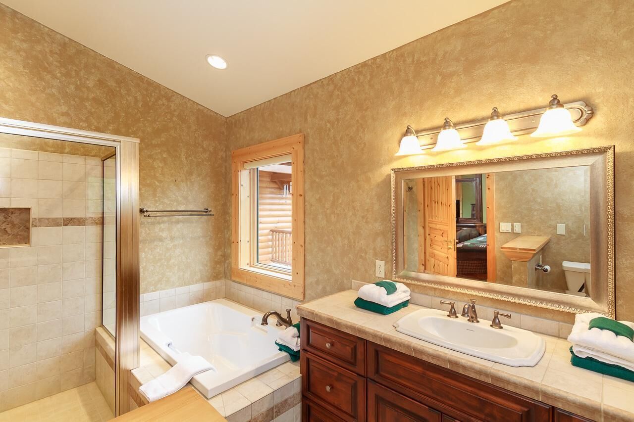 A bathroom with a glass shower enclosure, a bathtub, a vanity with a mirror, and a sink.