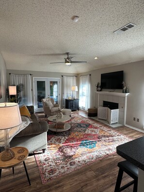 Ein Wohnzimmer mit Sofa, Couchtisch, Fernseher, Kamin und Deckenventilator.