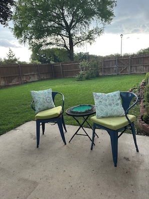 Eine Terrasse mit zwei Stühlen und einem kleinen Tisch, umgeben von einem Holzzaun und einem Rasen.