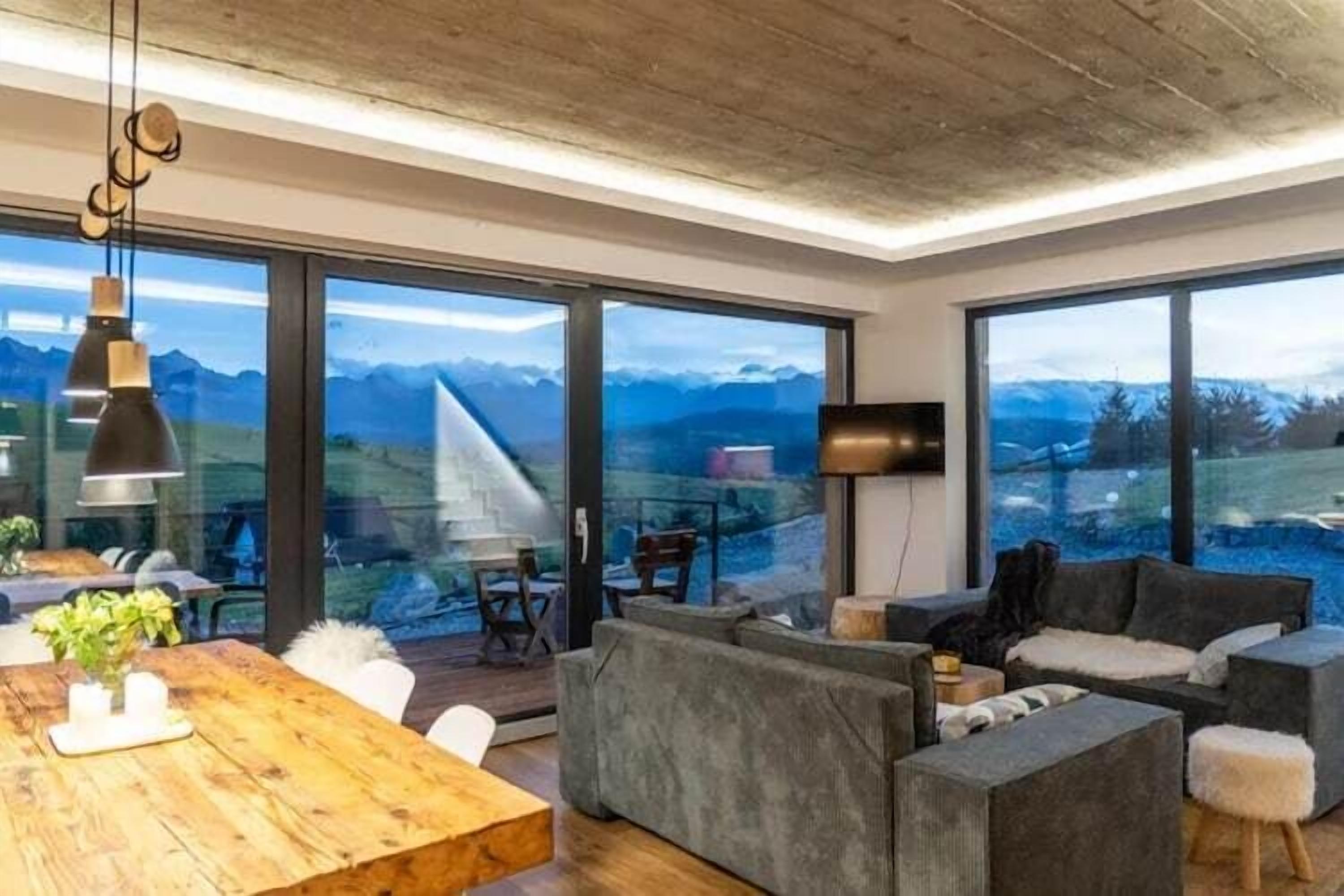 Un salon moderne avec de grandes fenêtres, une table à manger en bois et des canapés gris.