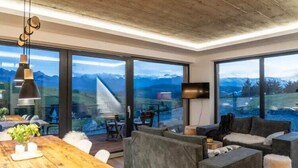 En moderne stue med store vinduer, et træspisebord og grå sofaer.