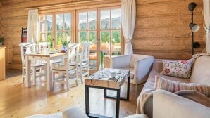 Un accogliente interno di una baita con zona pranzo, divano e vista panoramica attraverso ampie finestre.