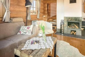 Ein gemütliches Blockhaus-Interieur mit einer Holz-Couch, einem Tisch mit Spitze-Tischdecke, einer Vase mit Blumen und einem Kamin.