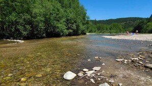 Une rivière aux eaux claires, bordée d’une végétation luxuriante, et une plage de sable parsemée de rochers.