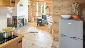L’intérieur d’une cabane en rondins, avec une cheminée, une table à manger, un réfrigérateur et un coin salon confortable.