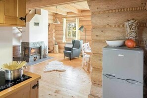 A log cabin interior with a fireplace, a dining table, a refrigerator, and a cozy seating area.