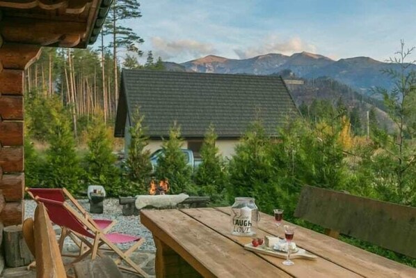 Una mesa de madera con un letrero, una silla roja y vista a una casa con la montaña de fondo.