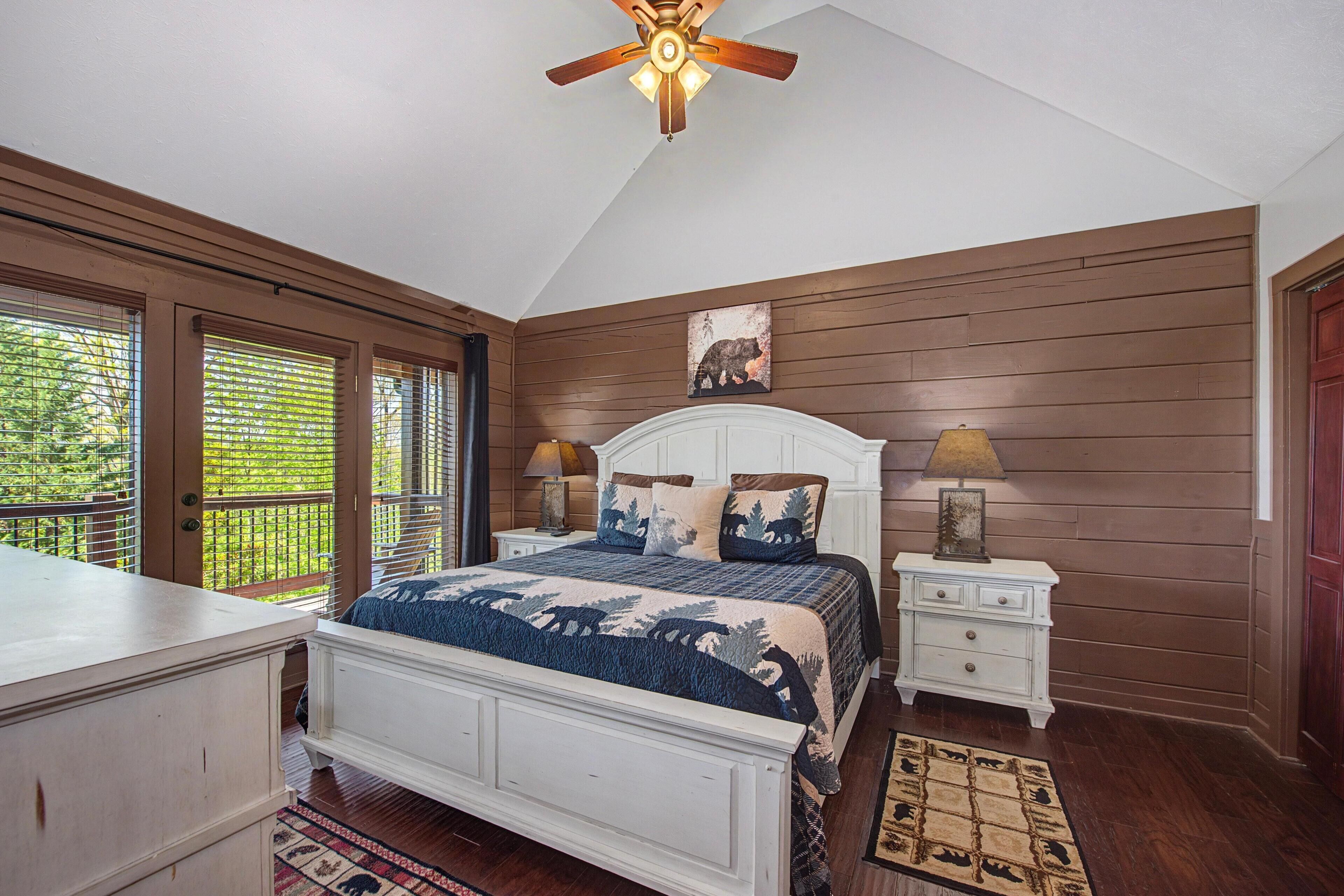 A bedroom with a bed, nightstands, a ceiling fan, a window with blinds, and a wooden wall panel.