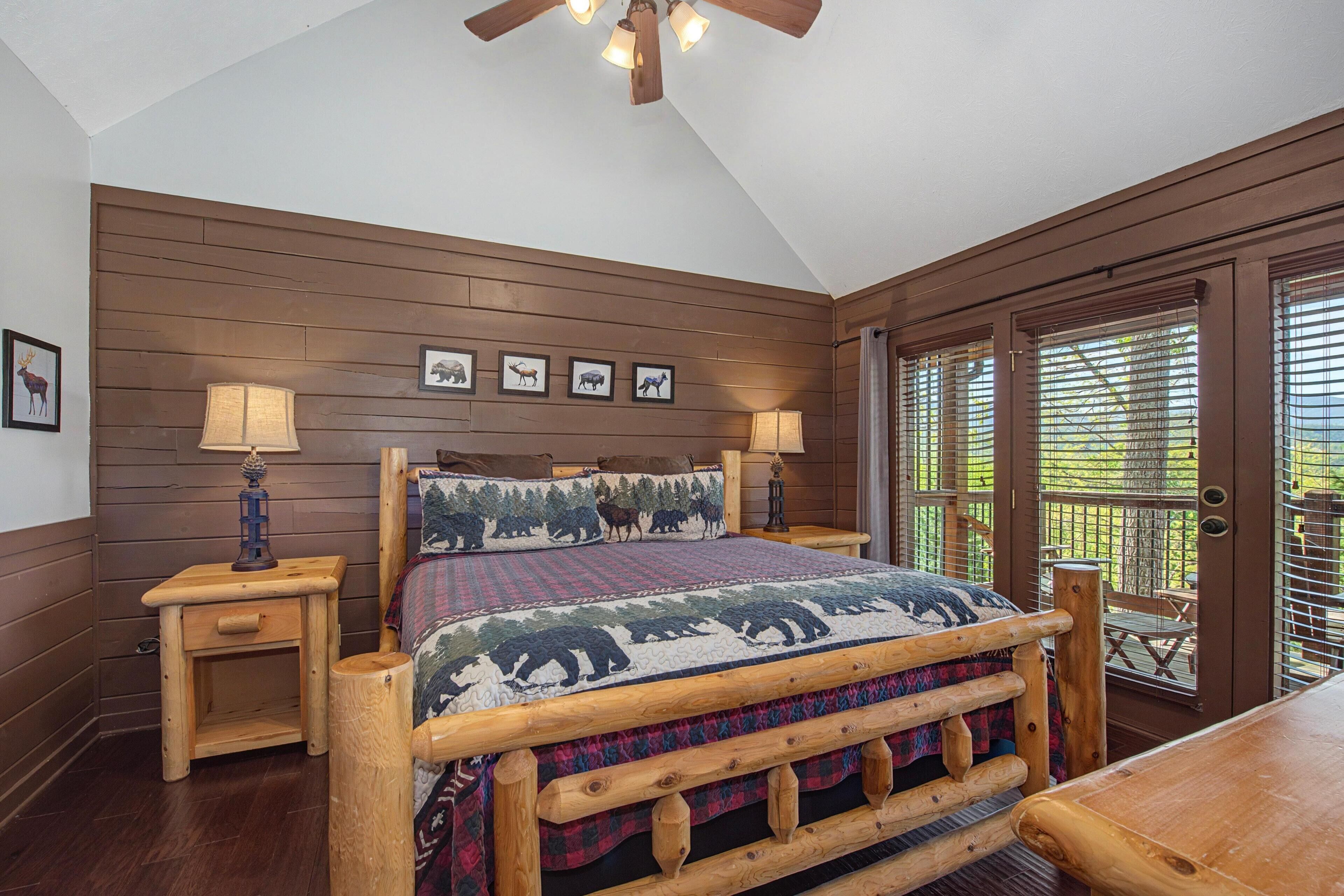 A bedroom with a wooden headboard, a quilt with animal prints, two bedside tables with lamps, and a view of the outdoors through a door with blinds.