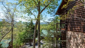 A log cabin with a stone wall, surrounded by trees and a view of a lake. - Another Day in Bearadise (Gatlinburg)