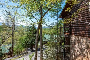 A log cabin with a stone wall, surrounded by trees and a view of a lake. - Another Day in Bearadise (Gatlinburg)