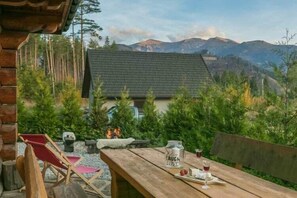 Una mesa de madera con un letrero, una silla roja y vista a una casa con la montaña de fondo.