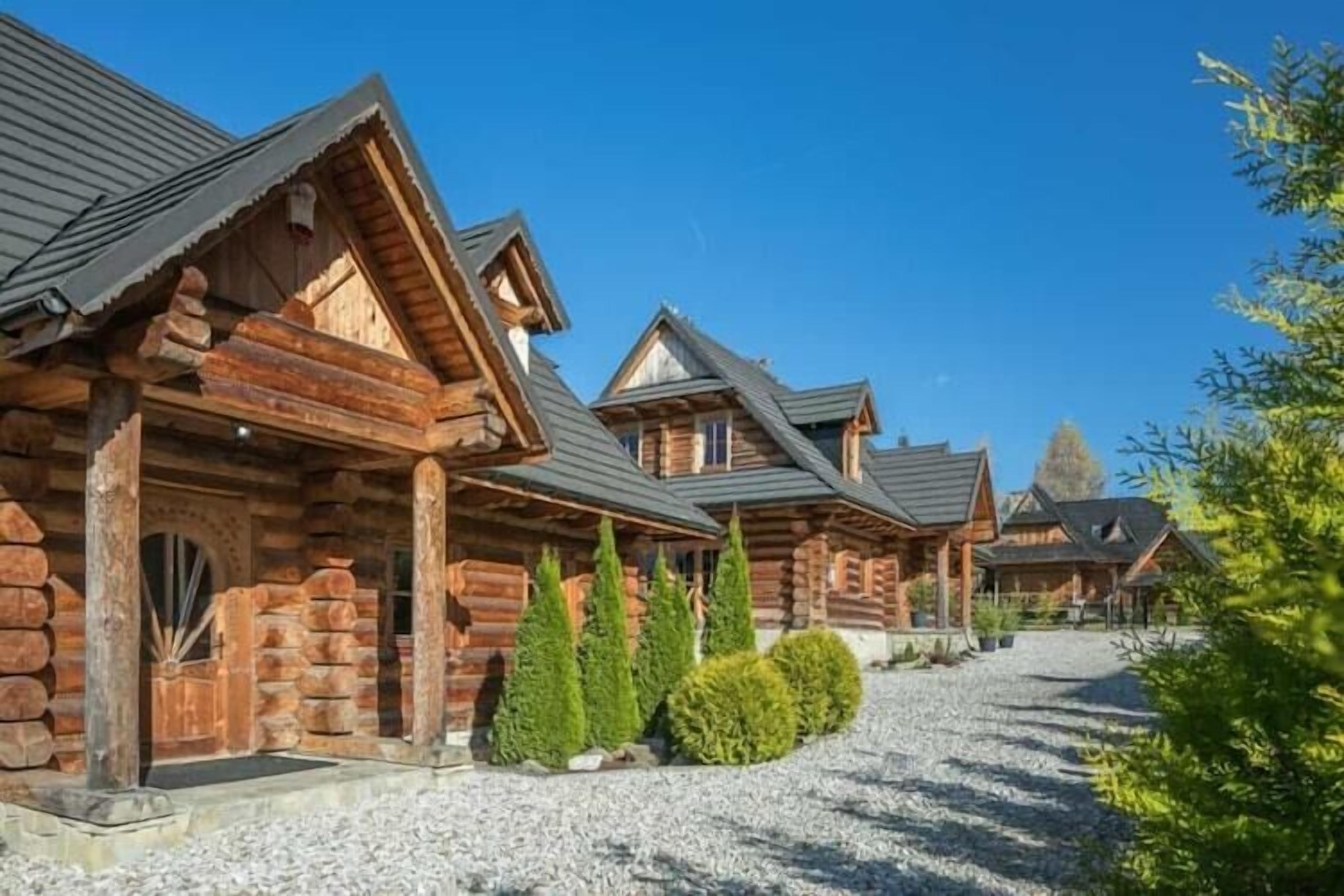 Une rangée de chalets en rondins, avec une allée en gravier et des arbustes soigneusement taillés.