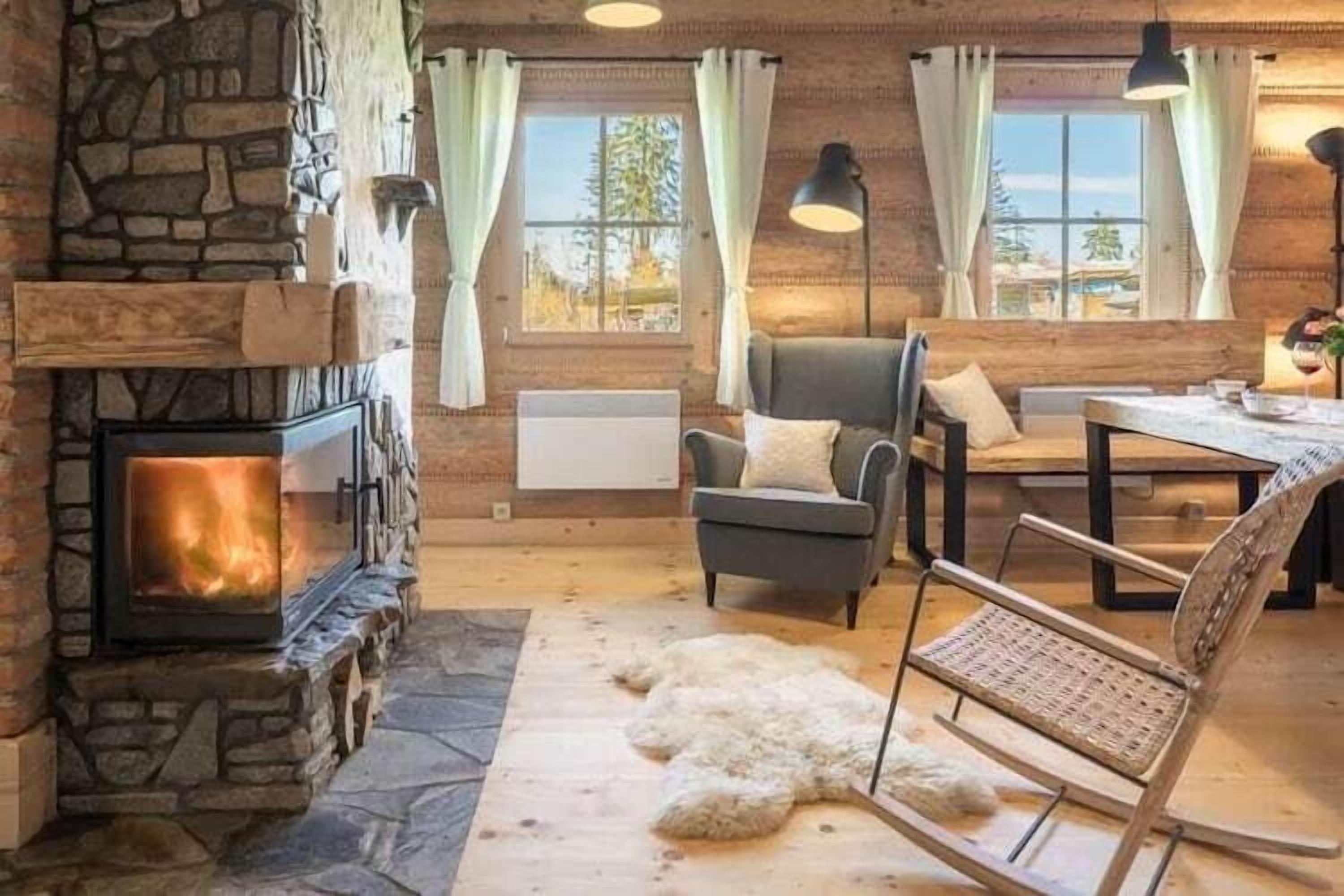 Une pièce chaleureuse avec une cheminée en pierre, un fauteuil confortable, une table à manger et une vue sur l’extérieur.