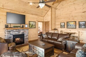 Ein gemütliches Wohnzimmer mit Kamin aus Stein, Ledermöbeln, einem Flachbildfernseher und gerahmten Kunstwerken an den Wänden.