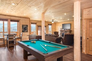 Un interior de madera con mesa de billar, zona de estar y televisor.