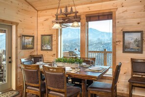 A wooden interior with a dining table set for six, surrounded by chairs, with mountain views through large windows. - Bear and Trout (Gatlinburg)