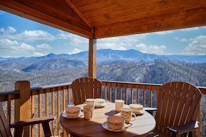 Una terraza de madera con una mesa y sillas, con vista a un paisaje montañoso.