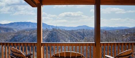 A wooden deck with Adirondack chairs overlooking a mountainous landscape.