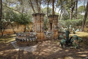 An ancient stone structure with columns and a circular stone basin, surrounded by cacti and trees. - Villa del Prete by Casa di Marco (Nardò)