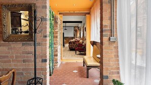 Un couloir avec un mur en briques, un miroir, un banc et une porte donnant sur une pièce où se trouvent un tapis à motifs et des meubles.