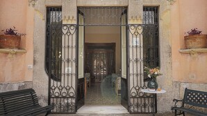 Una entrada con puertas de metal ornamentadas, un banco y una planta en maceta.