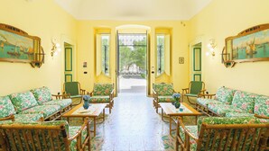 Una habitación con sofás y sillones de estampado floral, suelo de baldosas y vistas a través de una puerta abierta.