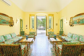 Ein Zimmer mit Sofas und Sesseln mit Blumenmuster, einem gefliesten Boden und Blick durch eine offene Tür.