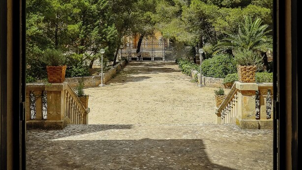 Una entrada con reja a un patio con un camino empedrado que lleva a un edificio.