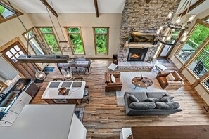 Un vaste espace de vie agrémenté d’une cheminée en pierre, de parquets en bois et de grandes fenêtres offrant une vue sur la verdure.