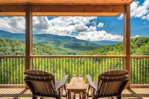 A wooden deck with two chairs and a table, overlooking a mountainous landscape. - The Perfect Tenn (Gatlinburg)